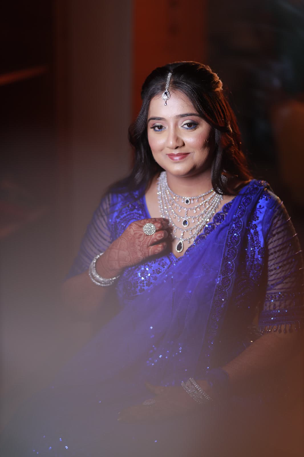 Woman in royal blue saree seated against a dark studio backdrop