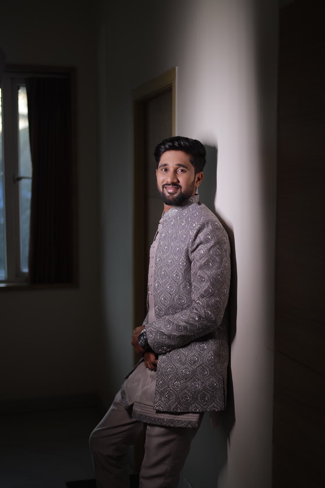 Man in sherwani leaning against a stone pillar